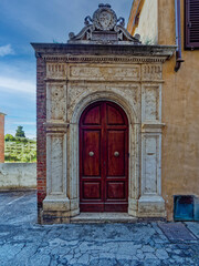 Ornate arched wooden door in Siena, Tuscany, Italy, set within a carved stone doorway. The dark red...