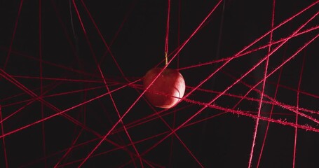 Approaching a red apple hanging inside a net of stretched red woolen threads on a black background. Concept of a cherished dream