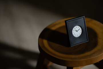 Minimal black clock on wooden stool in moody light