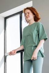 Woman in green outfit poses by window during natural light moment at home