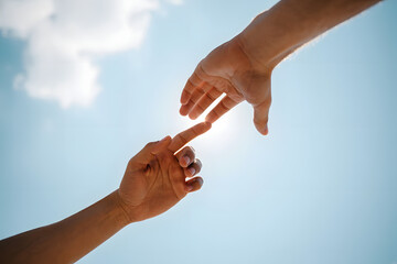 Two hands reach towards each other against a bright blue sky, symbolizing connection