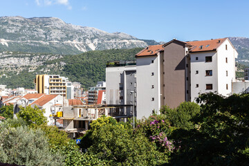 Obraz premium Modern apartment buildings surrounded by greenery in Budva, Montenegro, with scenic mountain panorama under clear blue sky