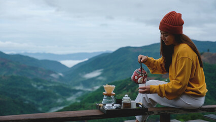 A woman pouring tea while sitting on wooden terrace and looking at a mountain view
