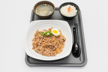 A savory beef rice bowl served as a set meal, featuring tender slices of beef simmered in soy-based sauce atop steamed white rice. The dish is accompanied by a variety of side vegetables and a light