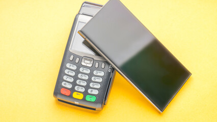 A black cell phone is placed on top of a black card reader. The card reader is rectangular in shape and has a silver color