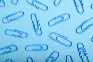 Many blue paper clips isolated on light blue background, flat lay