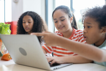 Diverse group of kids three girls happy looking at computer screen together, modern workspace. They...