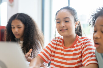 Diverse group of kids three girls happy looking at computer screen together, modern workspace. They...