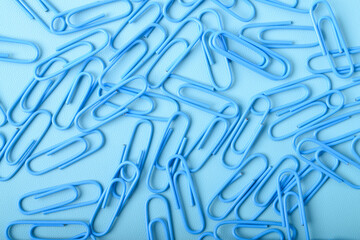 Many blue paper clips isolated on light blue background, flat lay