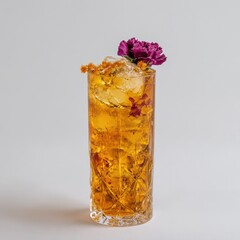 A tall, gold-toned cocktail garnished with a purple flower and edible golden-orange bits, sits atop ice