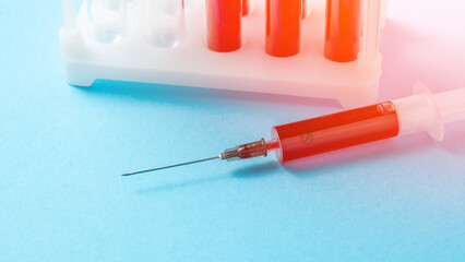 A syringe with a red liquid in it is on a blue background. The syringe is in a lab setting with other lab equipment