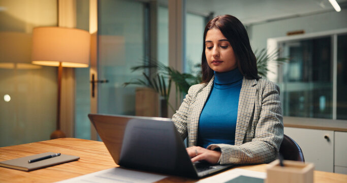 Laptop, night and typing with business woman in office for finance, investment or report deadline. Accounting, computer and financial review with Indian employee at desk in workplace for planning - Powered by Adobe