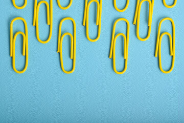 Many yellow paper clips isolated on light blue background, flat lay
