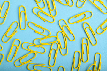 Many yellow paper clips isolated on light blue background, flat lay