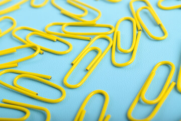 Many yellow paper clips isolated on light blue background