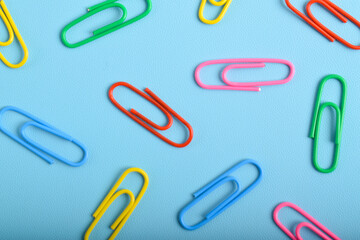 Colorful paper clips isolated on light blue background, flat lay, top view