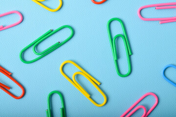 Colorful paper clips isolated on light blue background, flat lay, top view