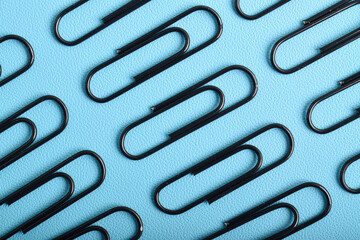 Many black paper clips isolated on light blue background, flat lay