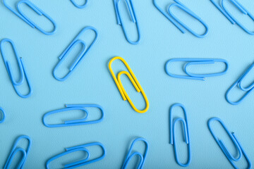 Yellow paper clip among blue ones on light blue background, top view. Difference, individuality, uniqueness
