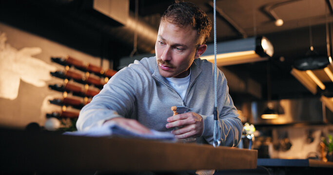 Man, bartender and cleaning with counter in cafe for detergence, disinfectant or preparation. Male person, cleaner or bottle with spray or chemical for dirt, bacteria or germ removal in coffee shop - Powered by Adobe