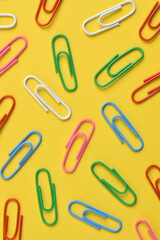 Colorful paper clips isolated on yellow background, flat lay, top view