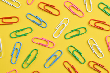Colorful paper clips isolated on yellow background, flat lay, top view