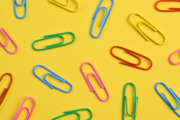 Colorful paper clips isolated on yellow background, flat lay, top view