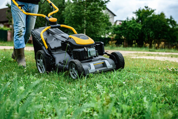 Gardener mowing green grass with yellow lawn mower in garden during summer day.