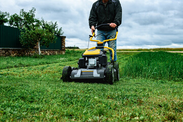 Gardener mowing green grass with yellow lawn mower in garden during summer day.