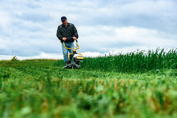 Gardener mowing green grass with yellow lawn mower in garden during summer day.
