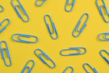Many blue paper clips isolated on yellow background, flat lay