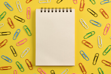 Blank notebook and paper clips on yellow background, flat lay. Space for text
