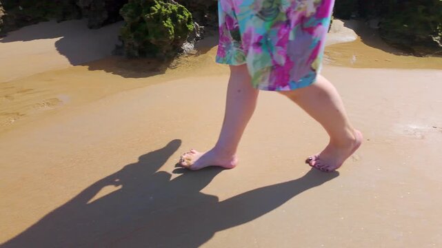 Bare feet of a woman walking on the sand of the beach and putting her feet in the small pools of water