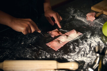 Woman Preparing Homemade Ravioli with Red Pasta Dough in Rustic Kitchen Setting
