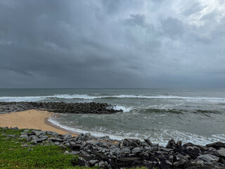 View of a beach with waves ,sand ,rocks ,greenery and blue sky.