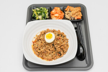 A Thai basil minced pork set meal arranged on a tray, including a portion of stir-fried spicy basil pork, a bowl of steamed white rice, three side vegetables, and a bowl of soup. The presentation refl