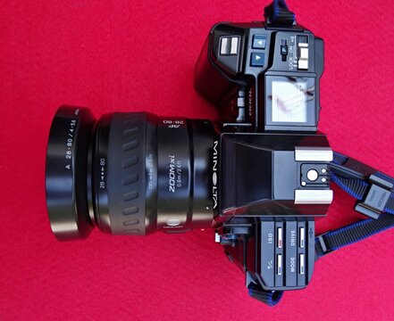 Minolta 7000i camera with zoom lens resting on red background