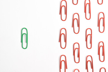 Green paper clip among red ones on white background, top view. Difference, individuality, uniqueness