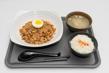 A Thai basil minced pork set meal arranged on a tray, including a portion of stir-fried spicy basil pork, a bowl of steamed white rice, three side vegetables, and a bowl of soup. The presentation refl