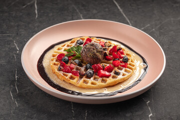 Waffle dessert with chocolate ice cream and fresh berries on pink plate