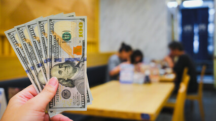 Consumers dine at a restaurant in a shopping mall with higher bills against a blurry background of...