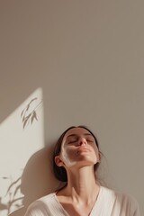 Woman relaxing with closed eyes under soft sunlight, face marked for advanced beauty treatment in serene setting

