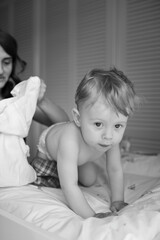 Mother gently dressing her baby sitting on a changing table. The baby looks around curiously while...