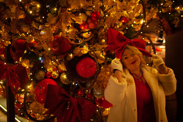 Plus size woman walks around the city during the Christmas of the week with a hot drink in a glass against the background of flickering light bulbs