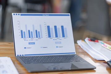 Computer laptop reviewing financial graphs and reports on desk.