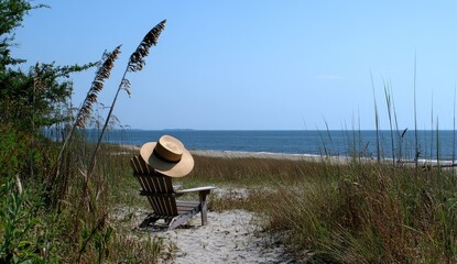 Beach chair with hat on a sandy path, ocean view