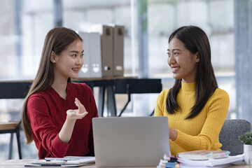 Two Asian businesswomen discussing work a digital laptop setting in a modern office.