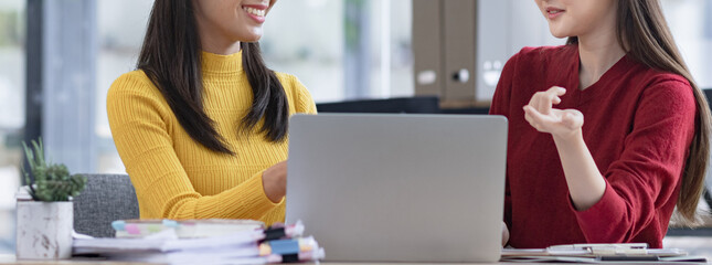 Two Asian businesswomen discussing work a digital laptop setting in a modern office.