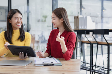 Two Asian businesswomen discussing work a digital tablet setting in a modern office, 