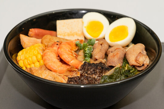 A hearty bowl of seafood noodle soup filled with shrimp, corn, egg, vegetables, rice blood cake, tofu skin, and assorted hotpot ingredients. The colorful ingredients float in a rich broth, making for 